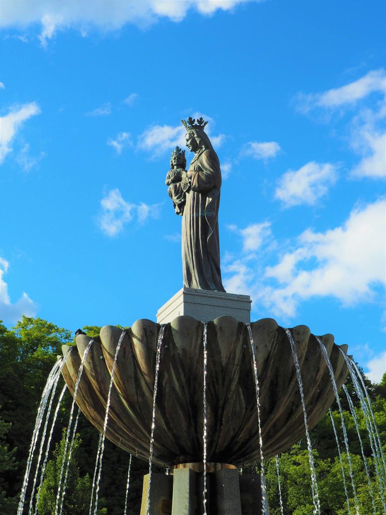 Graceful statue of Virgin Mary with Child atop a fountain under a blue sky in Sainte-Anne-de-Beaupré, Canada.